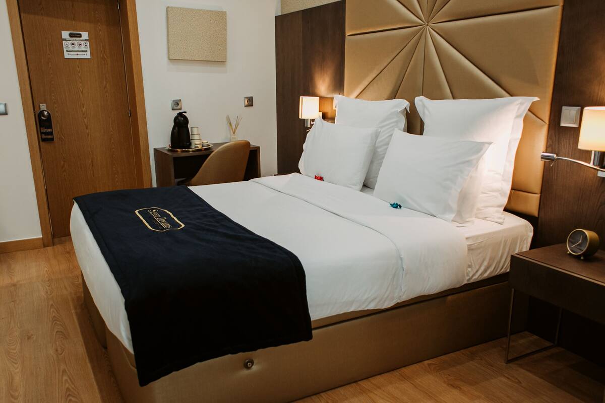 A hotel room with a bed, bedside tables, a nightstand, a wall-mounted clock, and a door with a keycard reader.