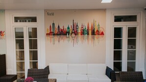 A room with a white sofa, wicker chairs, a glass table, and a wall mural of a city skyline. - Seven Dreams Suites (Lisbon)