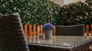 A wicker table with a glass top, a potted plant with purple flowers, and a small candle. - Seven Dreams Suites (Lisbon)