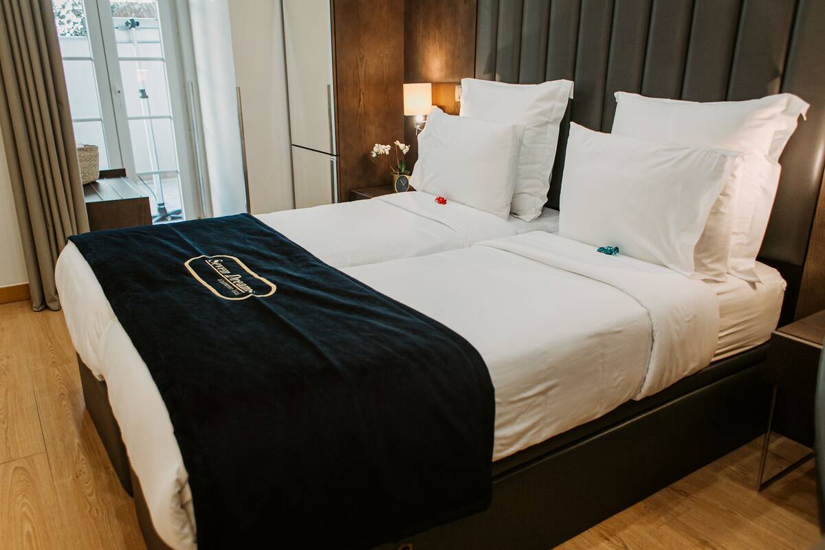 A double bed with a black and white bedspread, a wooden headboard, and a bedside table with a lamp and flowers.