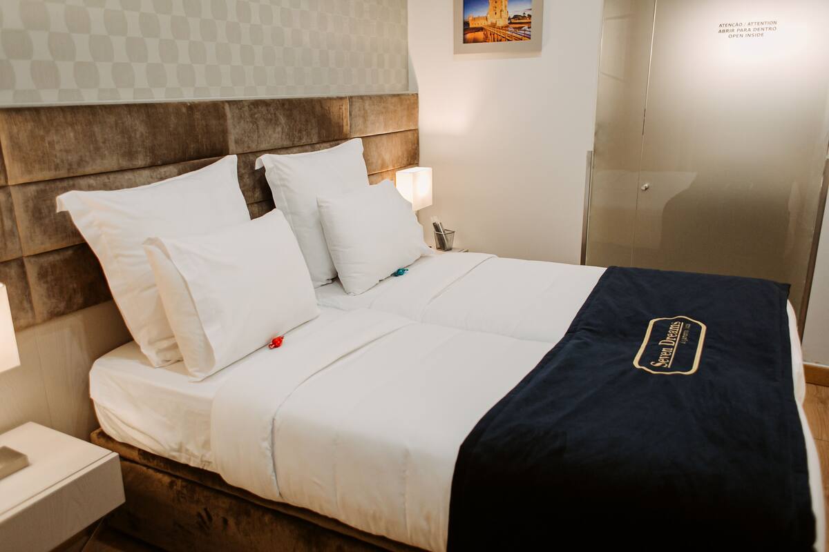A neatly made bed with white linens and a navy blue blanket, a bedside lamp, and a framed picture on the wall.