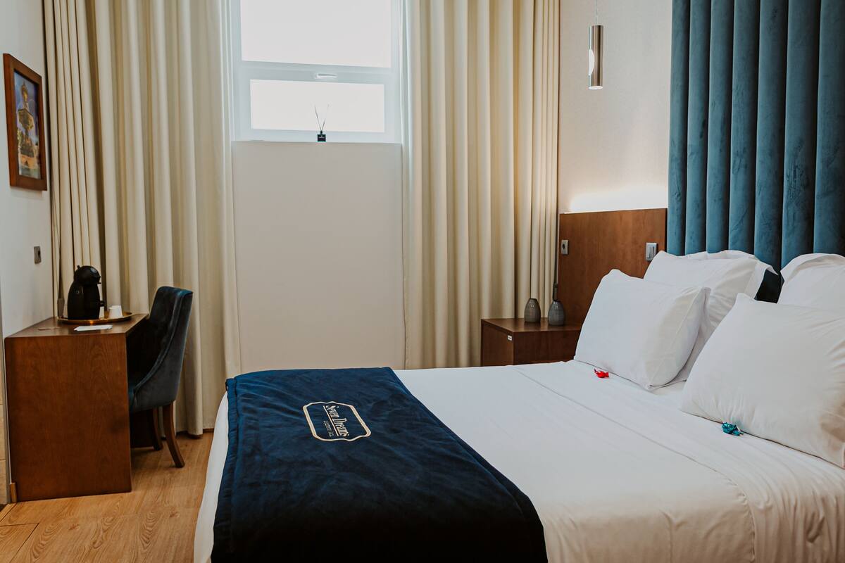 A hotel room with a bed, a desk, a chair, and a window.