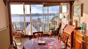 A dining area with a view of a body of water, a round table with a colorful tablecloth, and wooden furniture. - Studio sea view in Trégastel with private parking (Trégastel)