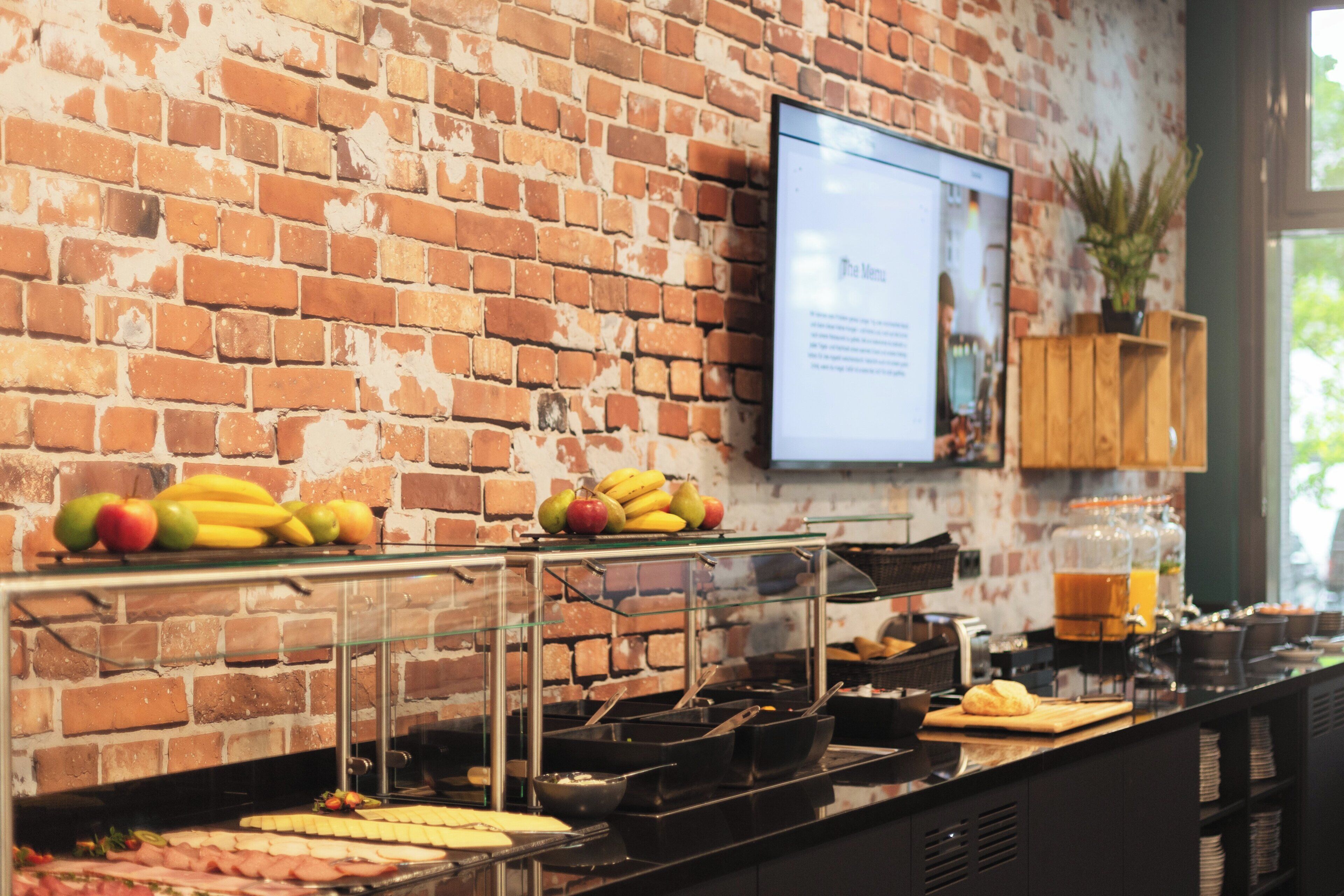 A buffet area with a brick wall, a television screen, and various food items.