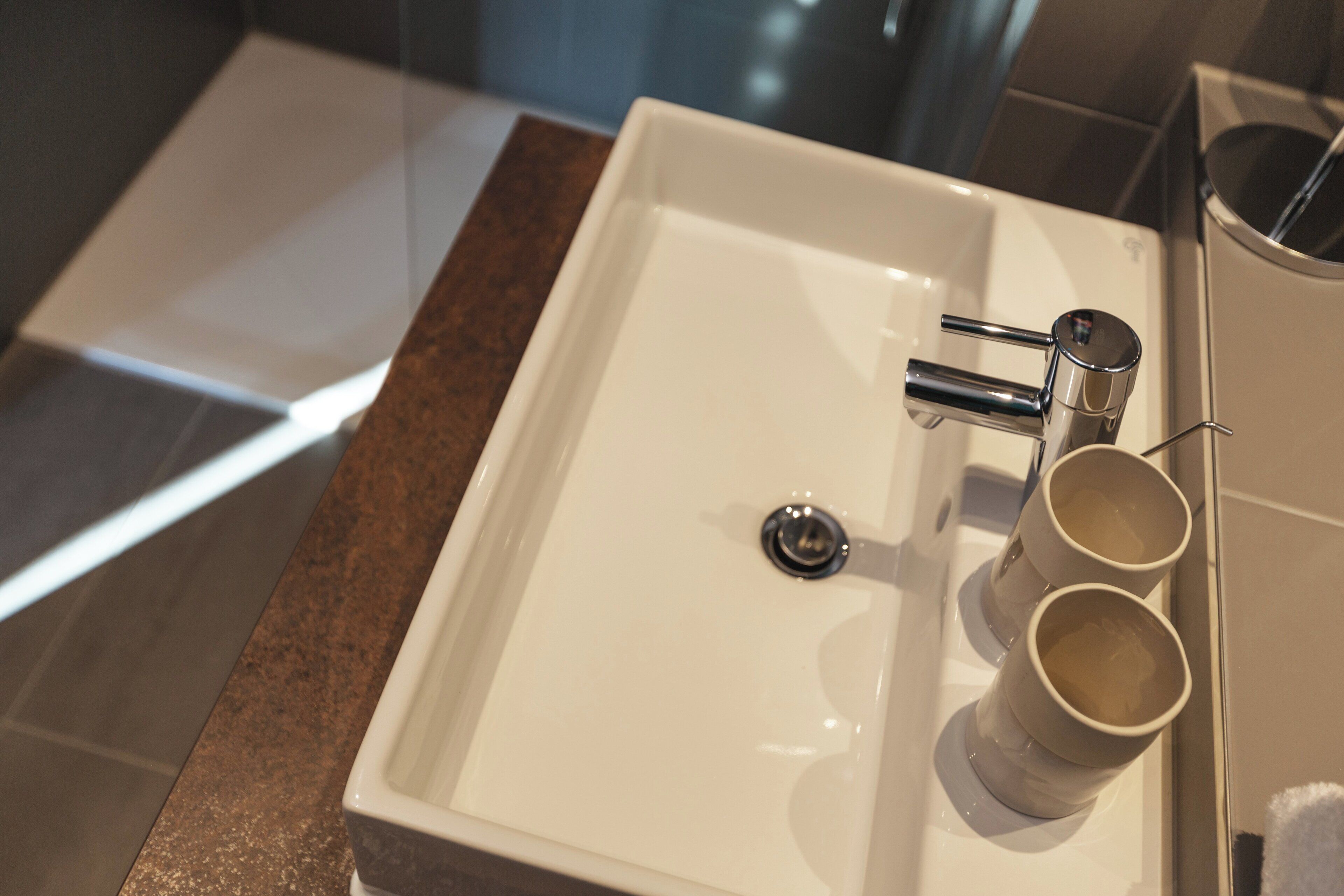Un lavamanos de baño con grifo cromado, un espejo y dos tazas sobre la encimera.