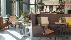 A modern interior with a brown sofa, round tables, and a seating area with a view of the city. - Holiday Inn - the niu, Bricks Hamburg by IHG (Hamburg)