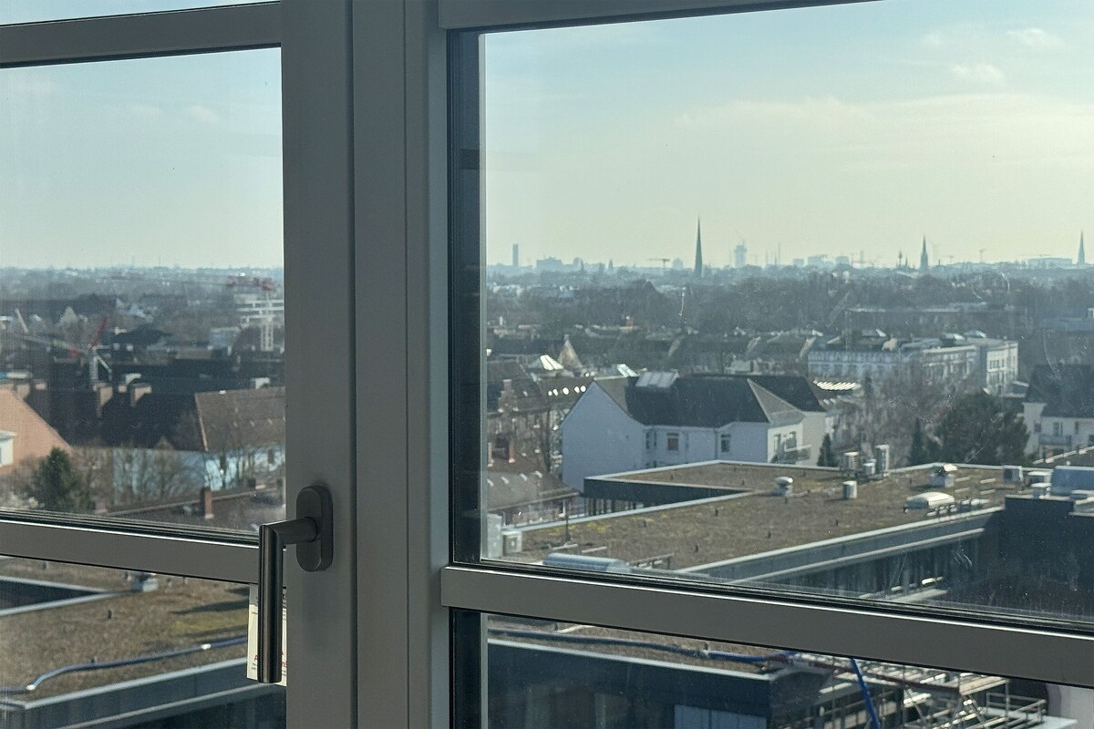 A window with a view of a cityscape, including buildings and a church spire.