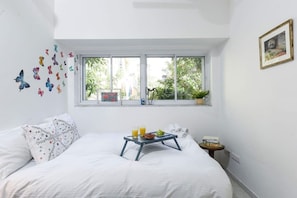 A bedroom with a bed, a window with a view of greenery, a small table with a tray, and a wall with butterfly decals.