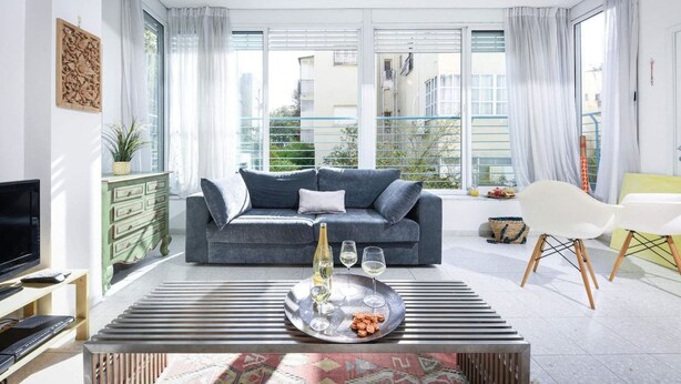 A modern living room with a sofa, a coffee table with a tray, and a television. - Luminous & Cozy 2BR — Your Stylish Urban Retreat (Tel Aviv-Yafo)