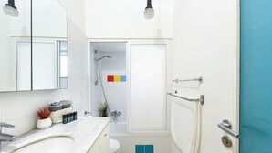 A bathroom with a white sink, a mirror, a towel rack, and a shower area. - Luminous & Cozy 2BR — Your Stylish Urban Retreat (Tel Aviv-Yafo)