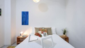 A bedroom with a bed, bedside tables, a lamp, a painting, and a potted plant. - Luminous & Cozy 2BR — Your Stylish Urban Retreat (Tel Aviv-Yafo)