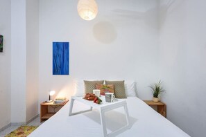 A bedroom with a bed, bedside tables, a lamp, a painting, and a potted plant.