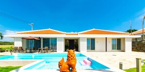 A modern house with a swimming pool, a patio with outdoor furniture, and a large statue of a bull.