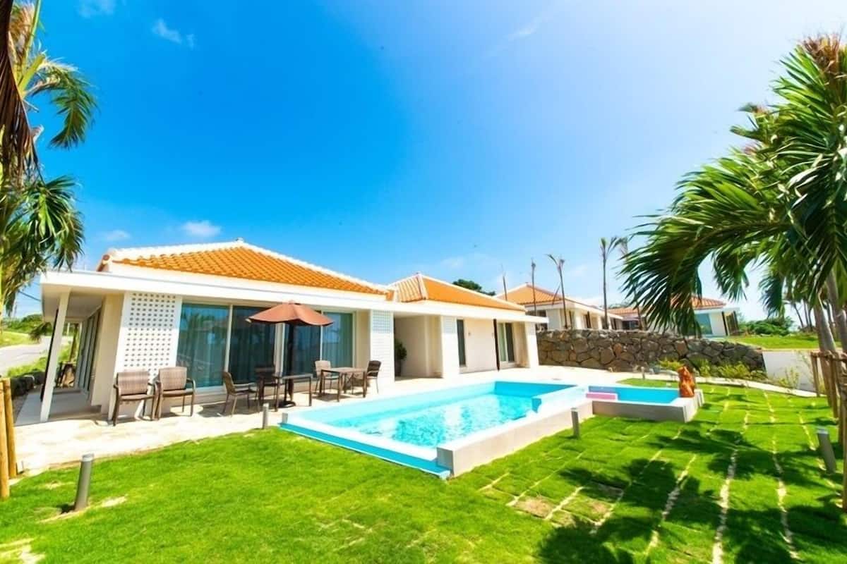 Ein modernes Haus mit Schwimmbad, einer Terrasse mit Stühlen und einem gepflegten Rasen.