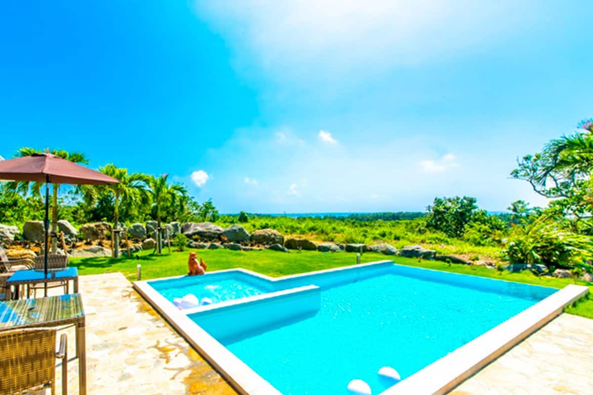 Ein Pool mit Liegestühlen und einem Tisch, umgeben von einem Garten und Blick auf den Ozean.