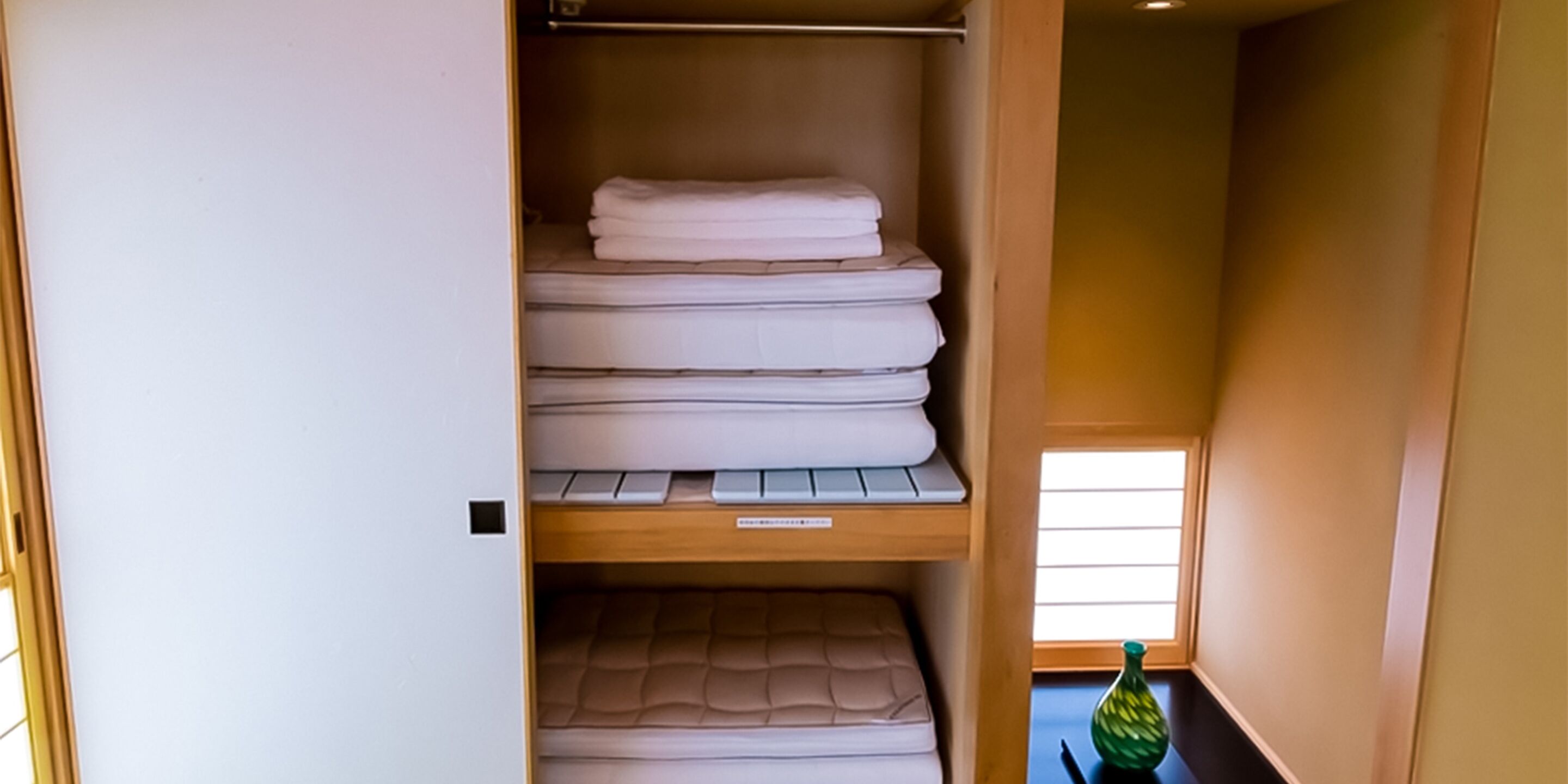 A room with a bed, a shelf with folded towels, and a small window.