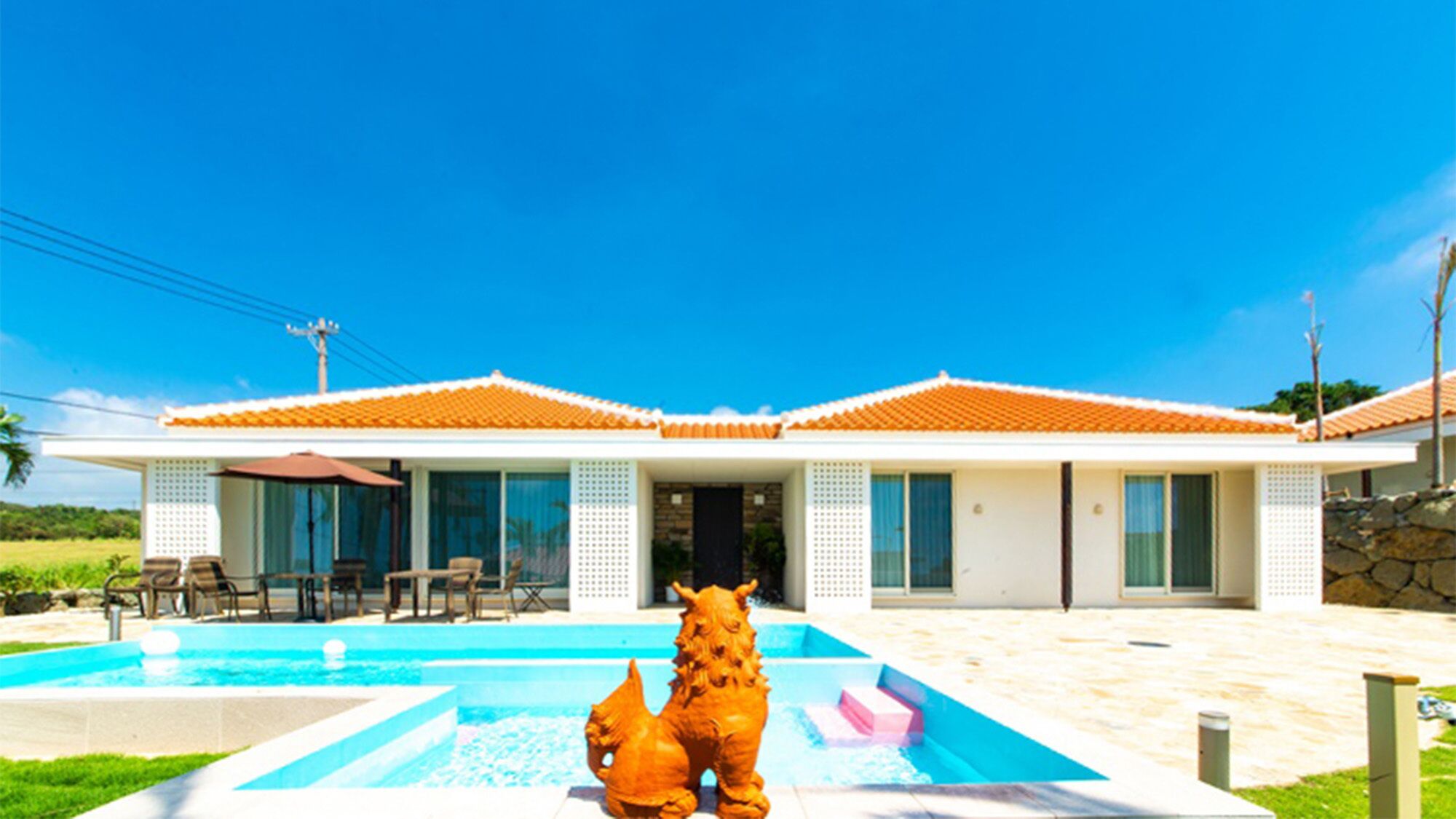 Una casa moderna con piscina, dos esculturas decorativas de animales y un patio con mobiliario de exterior.
