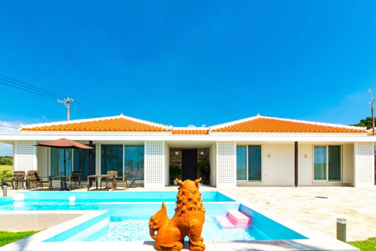 Ein modernes Haus mit Schwimmbad, zwei dekorativen Tiermedaillons und einer Terrasse mit Gartenmöbeln.