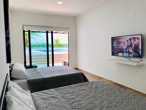 Quarto de hotel com duas camas, uma televisão fixada na parede e uma porta de vidro deslizante que dá para uma área de piscina.