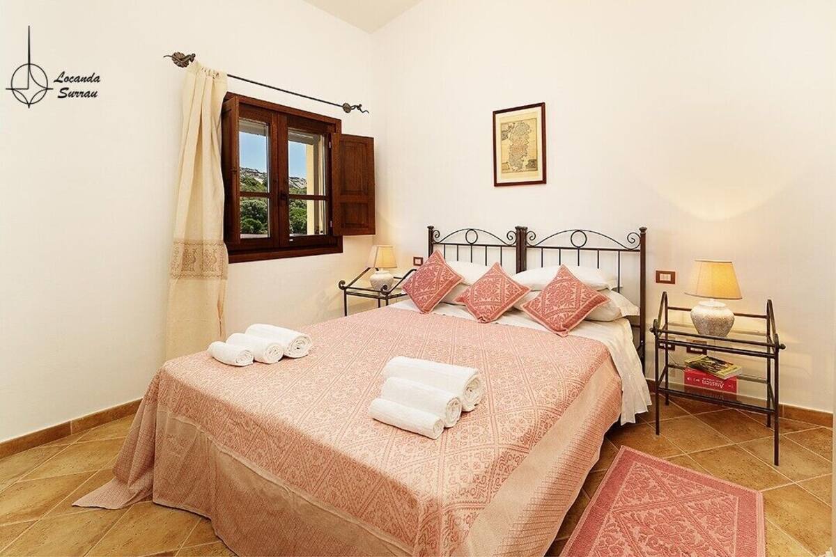 A neatly arranged bedroom with a bed, two bedside tables, a window with curtains, and a framed picture on the wall.