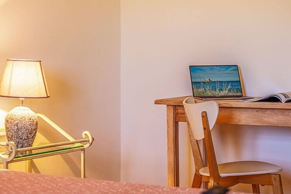 A bedroom with a bed, a bedside lamp, a wooden desk, a chair, and a painting on the wall.