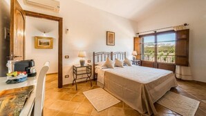A bedroom with a bed, bedside tables, a desk with a chair, a window with curtains, and a door. - Locanda In Vigna (Arzachena)