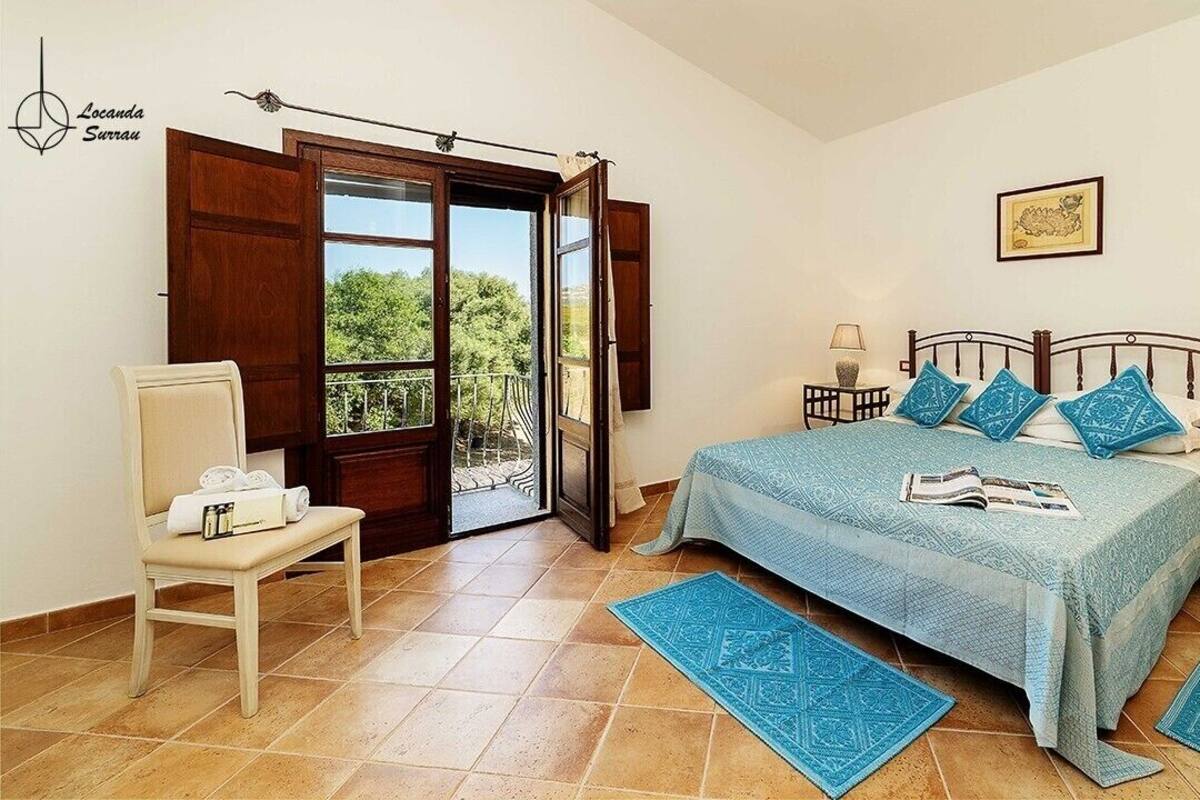 A bedroom with a bed, a chair, a nightstand, a lamp, and a window with a view of greenery.