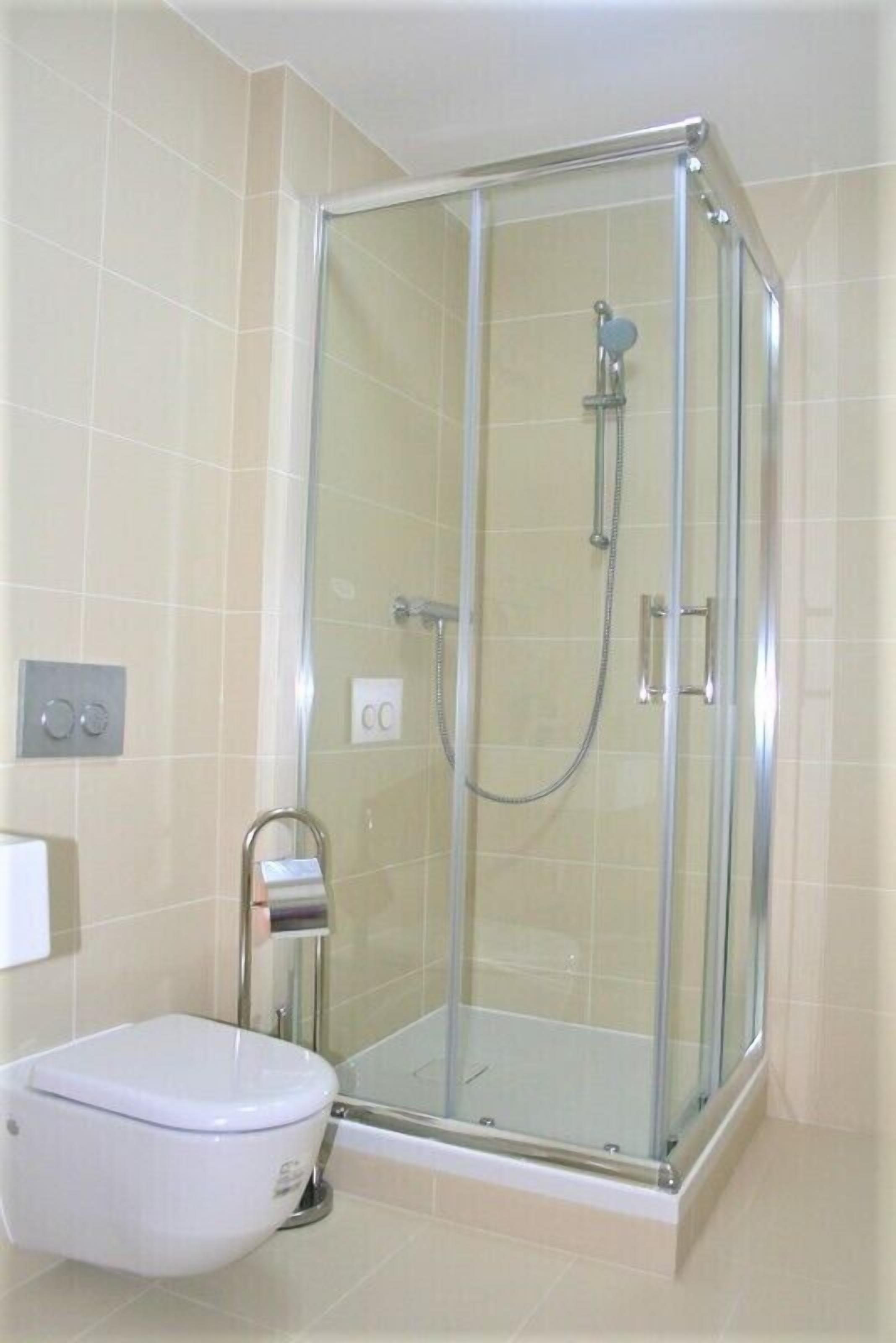 A glass-enclosed shower with a handheld showerhead and a wall-mounted faucet.