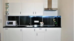 Una cocina moderna con armarios blancos, encimera negra, microondas y campana extractora de acero inoxidable.