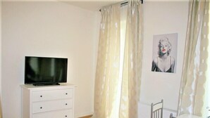 Una habitación con un aparador blanco, un televisor de pantalla plana, un cuadro en la pared y un comedor con sillas.