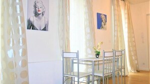 Un comedor con una mesa redonda y cuatro sillas, una planta en maceta y dos cuadros en la pared.