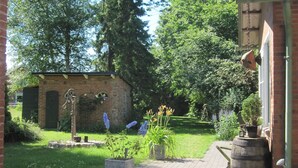A garden with a brick building, a wooden barrel, and a stone pathway. - Pottkiekerhus (Luhnstedt)