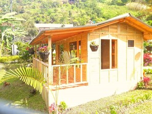 A wooden cabin with a porch, surrounded by lush greenery and a hilly landscape.