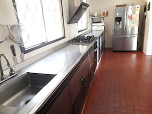 A kitchen with a stainless steel sink, a stove, and a refrigerator.