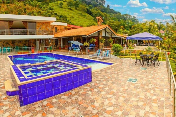 A pool area with a hot tub, lounge chairs, and a dining table.