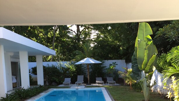Un espace aménagé au bord de la piscine, comprenant une piscine, des chaises longues, une table avec des boissons et une statue tiki.