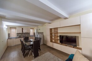 Una cocina moderna con comedor, un televisor de pantalla plana en la pared y un pequeño rincón de descanso con un cojín azul.
