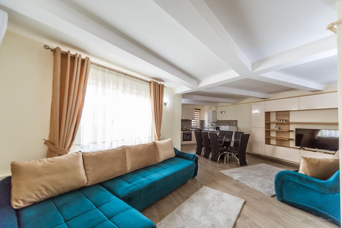 A modern living room with a sectional sofa, a TV, and a dining area with chairs and a table.