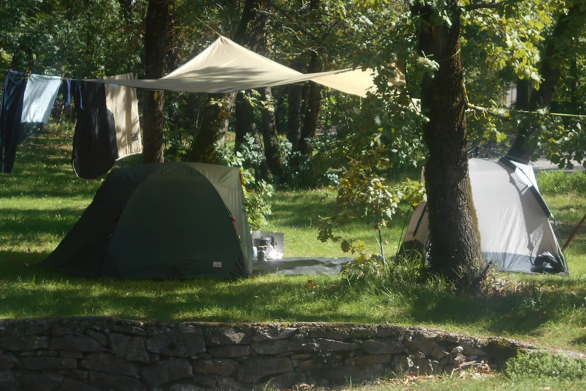 Un camping con dos tiendas de campaña, un tendedero con ropa y un muro de piedra al frente.