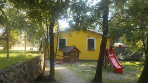 Un edificio amarillo con una pequeña estructura de madera y un tobogán rojo en un parque.