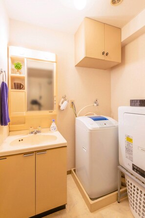 A compact bathroom with a sink, mirror, cabinet, and a white laundry machine.
