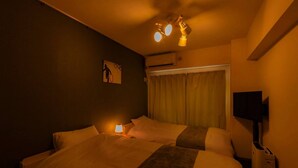 Een hotelkamer met een bed, een bedlamp, een airconditioning, een televisie en een raam met gordijnen.