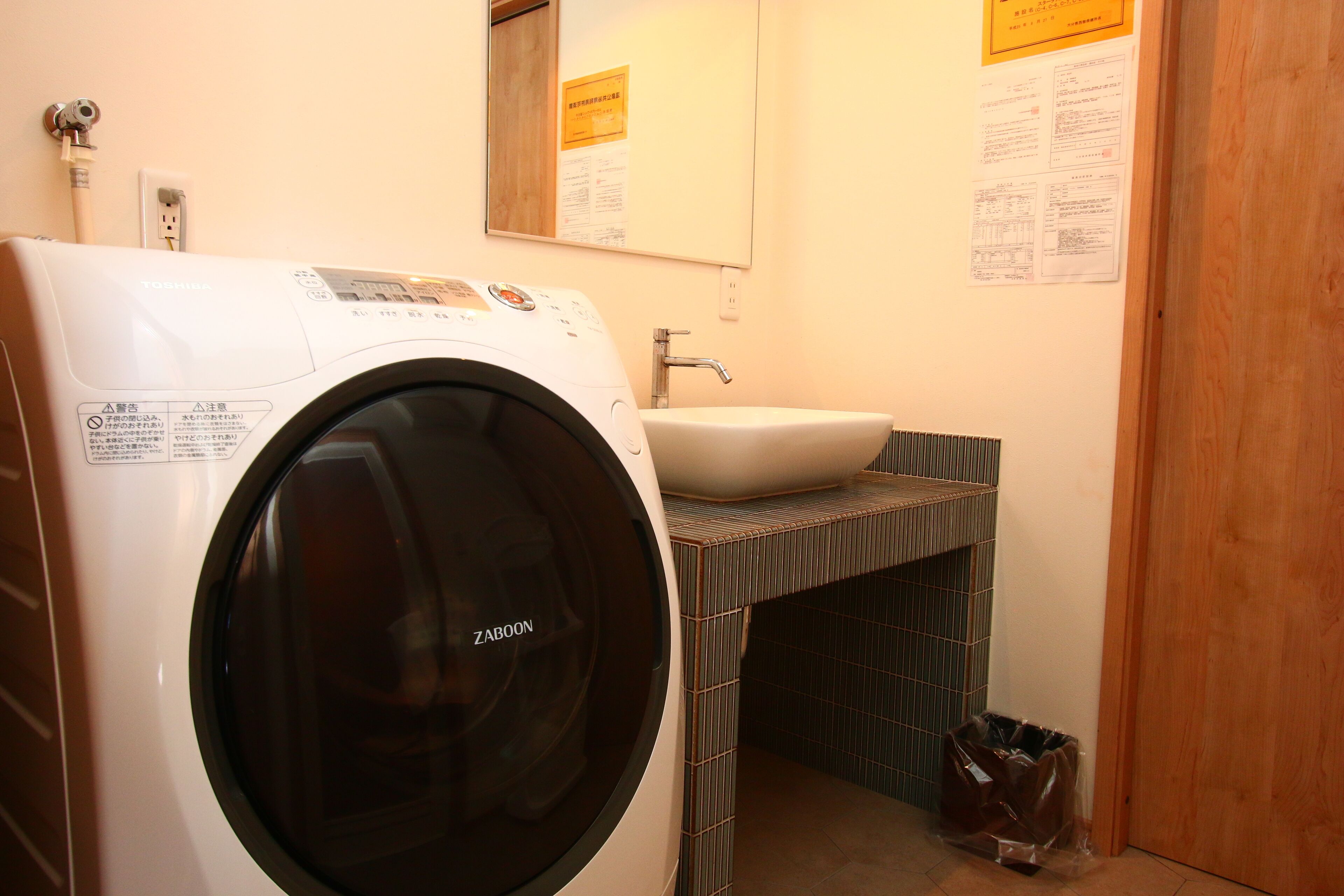 A compact hotel bathroom with a washing machine, a sink, and a mirror.