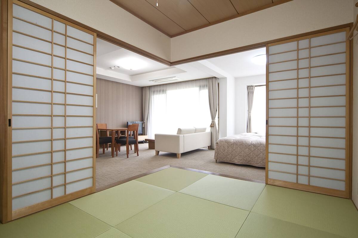 A traditional Japanese-style room with tatami flooring, a low table with chairs, a sofa, and a bed.