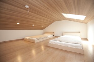 Un dormitorio moderno y minimalista con dos camas individuales, suelo de madera y techo inclinado con tragaluz.