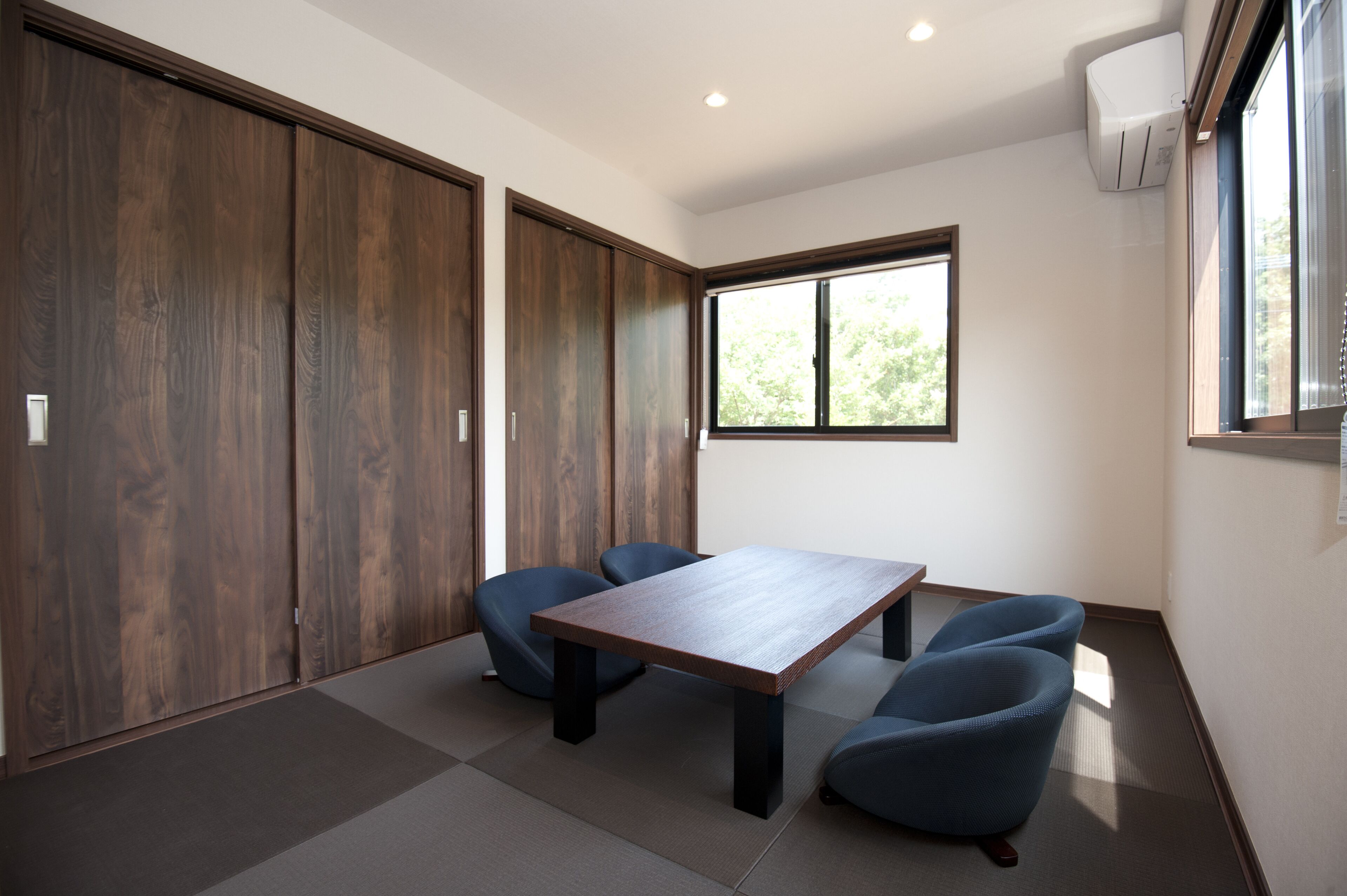 A room with a wooden table, four blue chairs, a sliding door, a window, and an air conditioning unit.