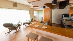 A modern kitchen with a wooden countertop, a built-in stove, and a sink. There are two rocking chairs and a small table with a plant. - GrandTree Hakone Sengokuhara (Hakone)