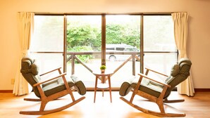 A room with two rocking chairs facing a large window, a small table with a plant, and a view of a vehicle outside. - GrandTree Hakone Sengokuhara (Hakone)