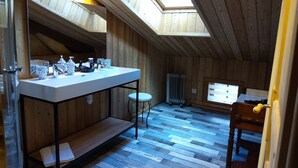 Interior de madera con tragaluz, un lavamanos blanco con artículos de aseo, un radiador y una ventana.