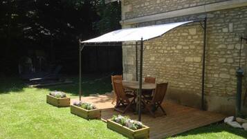 A patio area with a table and chairs, wooden planters with flowers, and a stone building in the background.